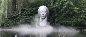 A large metal sculpture of a female head named "Leucantha", sits on water with mist at the sculpture's base at Rat's Restaurant.