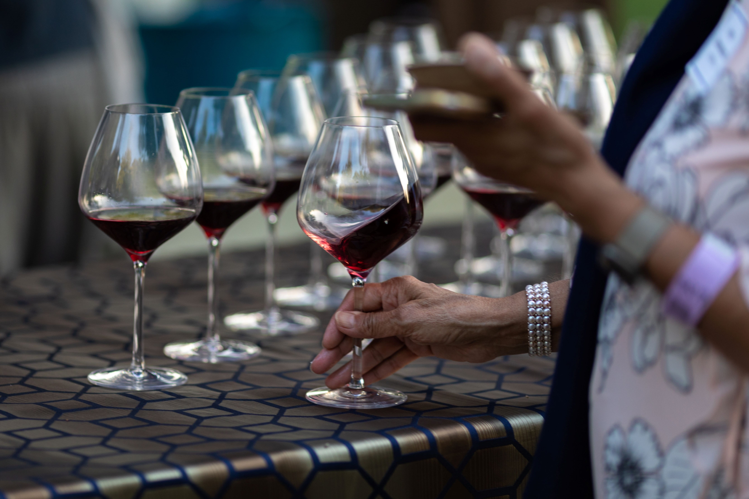 A woman picking up a glass of red wine from a display of glasses