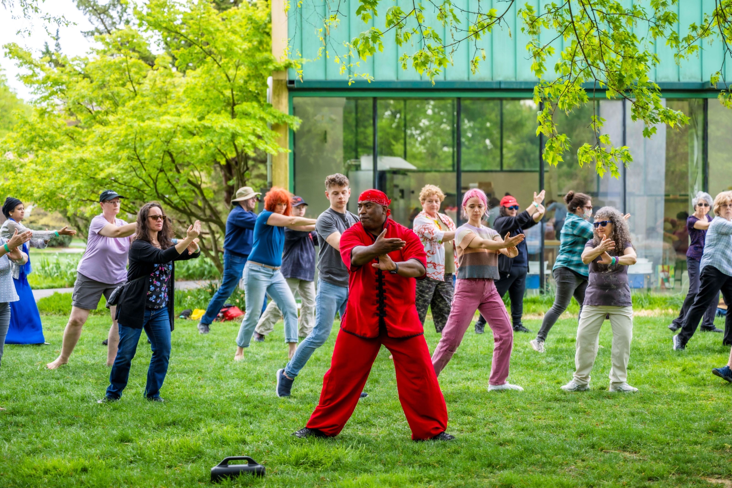 A man dressed in red leads a class of teenagers and adults in a Tai Chi exercise outdoors.