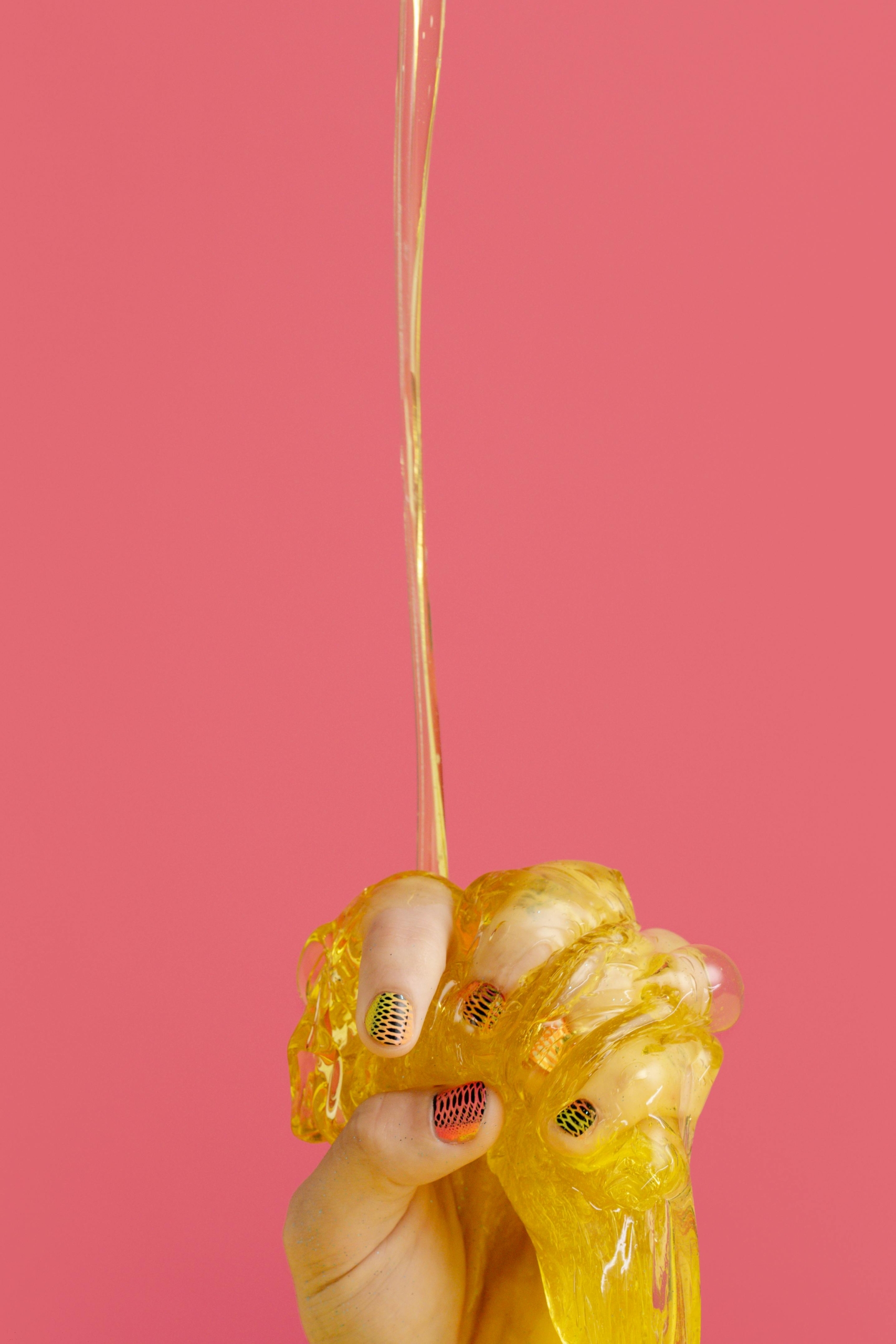 A hand covered in yellow slime in front of a pink background.