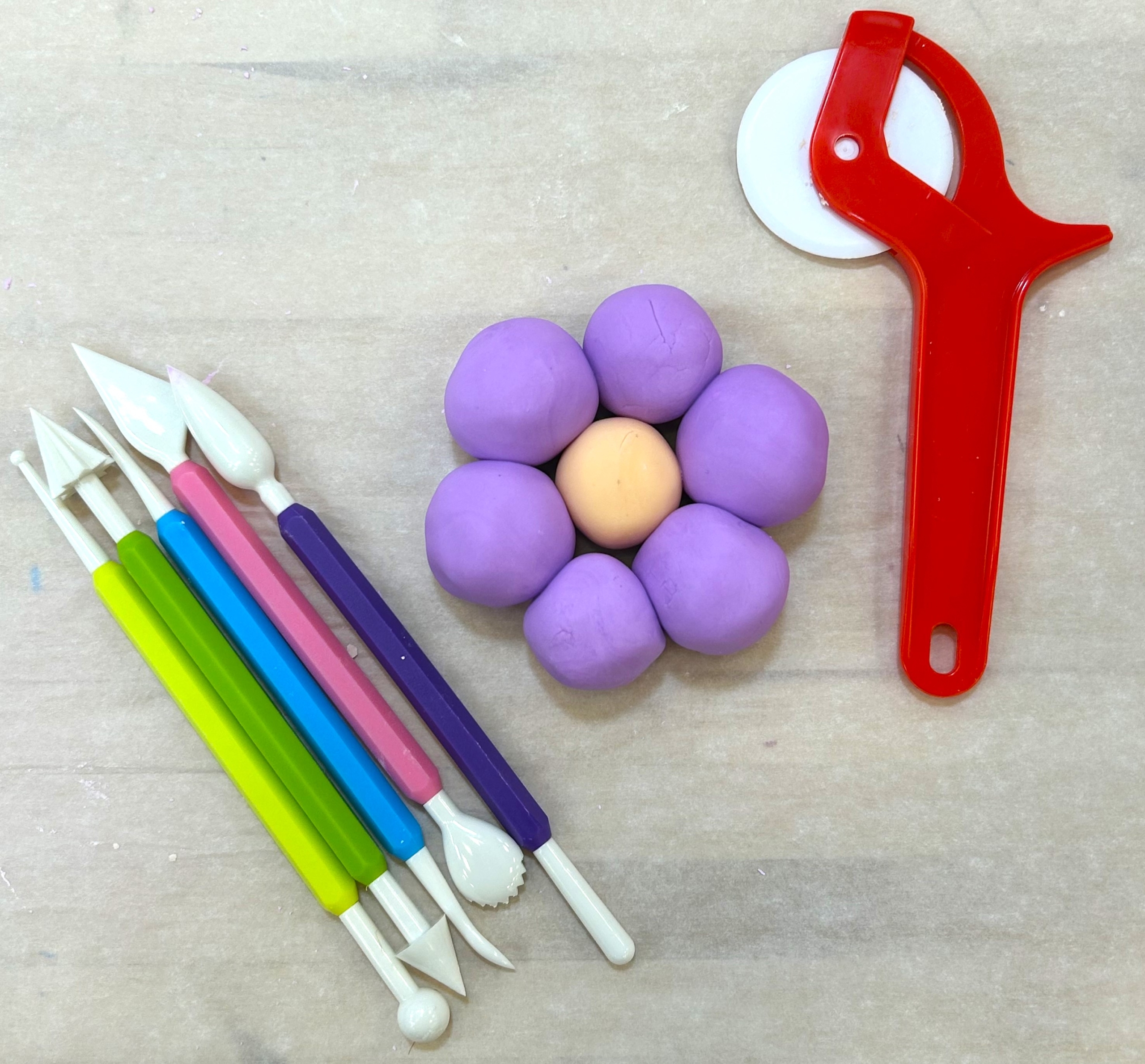 A purple and yellow flower made of cloud dough sits on a table around various tools used to shape clay.