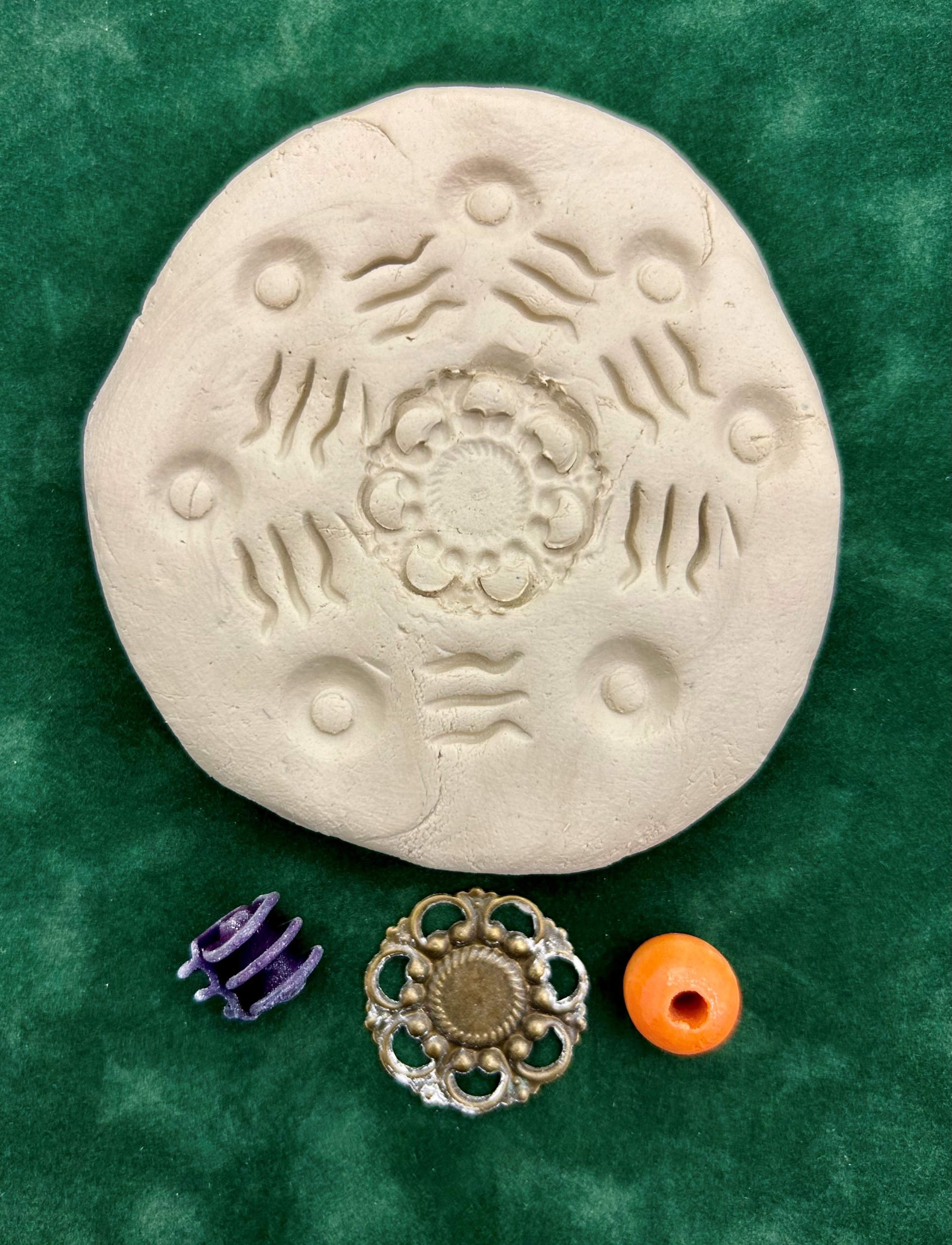 A circular piece of clay with impressions of three different objects pressed into it.