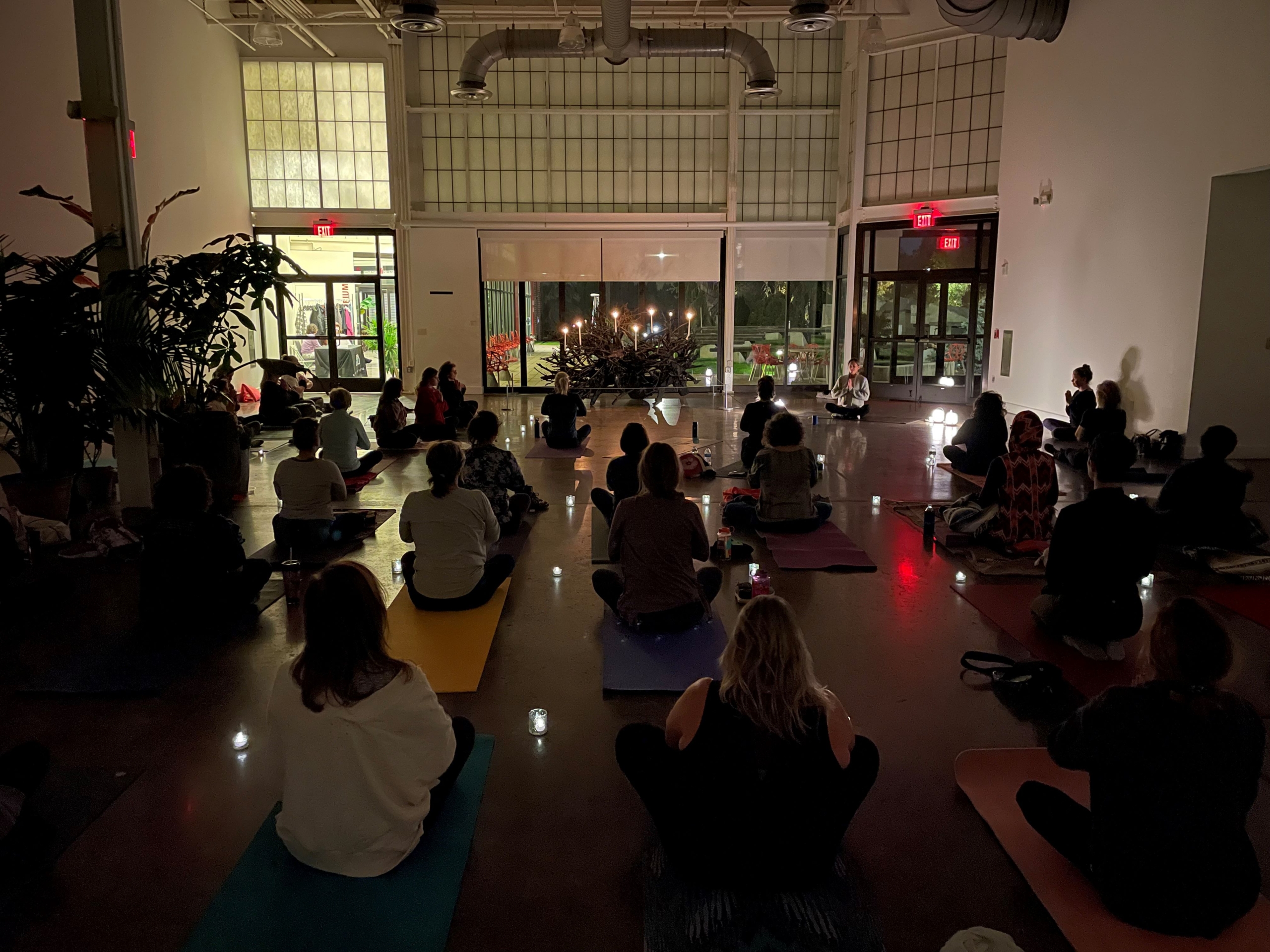 A dimly lit room of people doing yoga with candles next to them