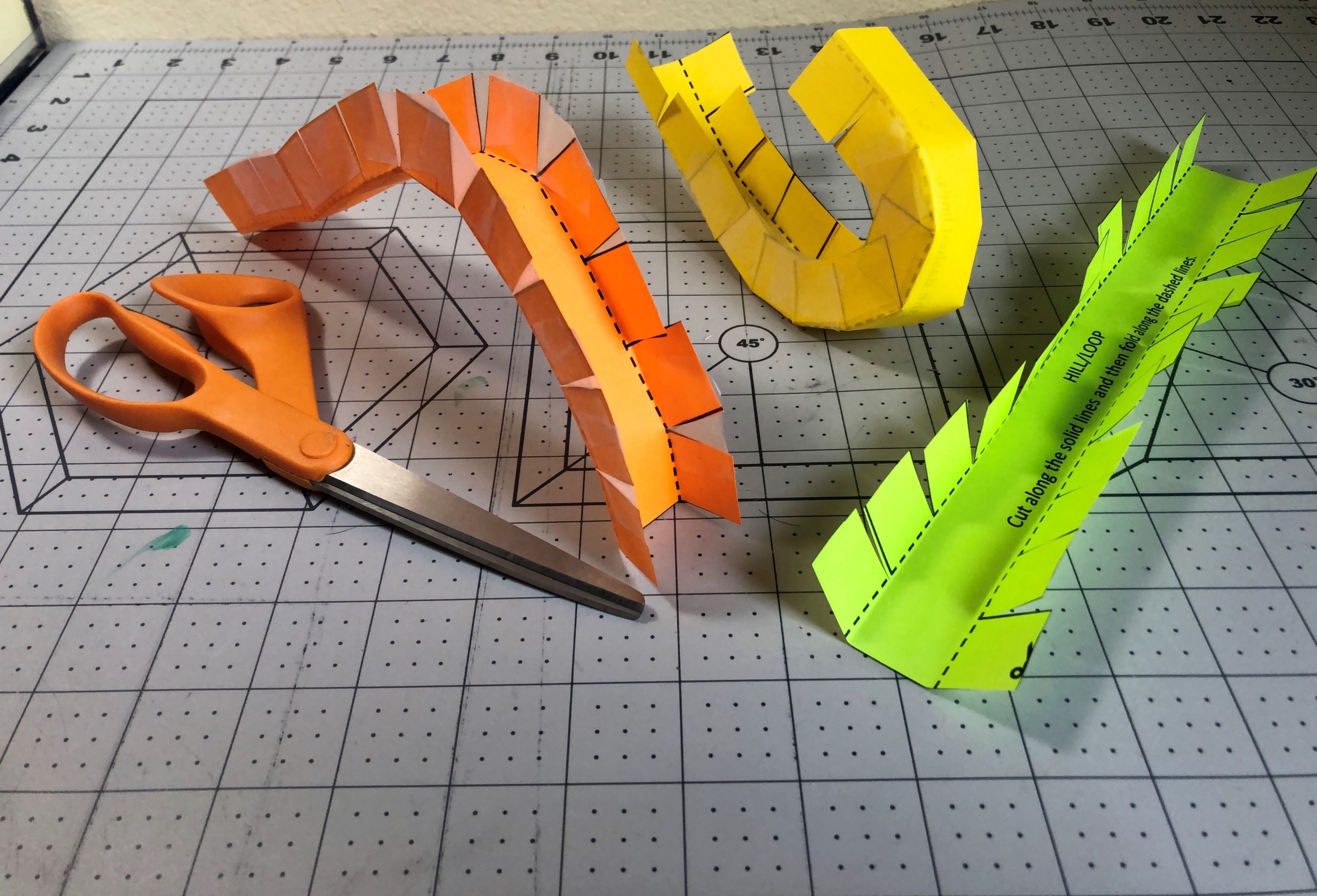 Three paper rollercoaster tracks made of orange, yellow, and green paper.