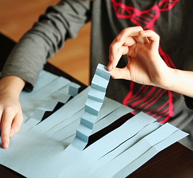 A child in a gray shirt making a foldable paper craft.