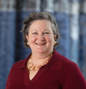 A headshot of Amy Gilman in a red shirt in front of a blue backdrop.
