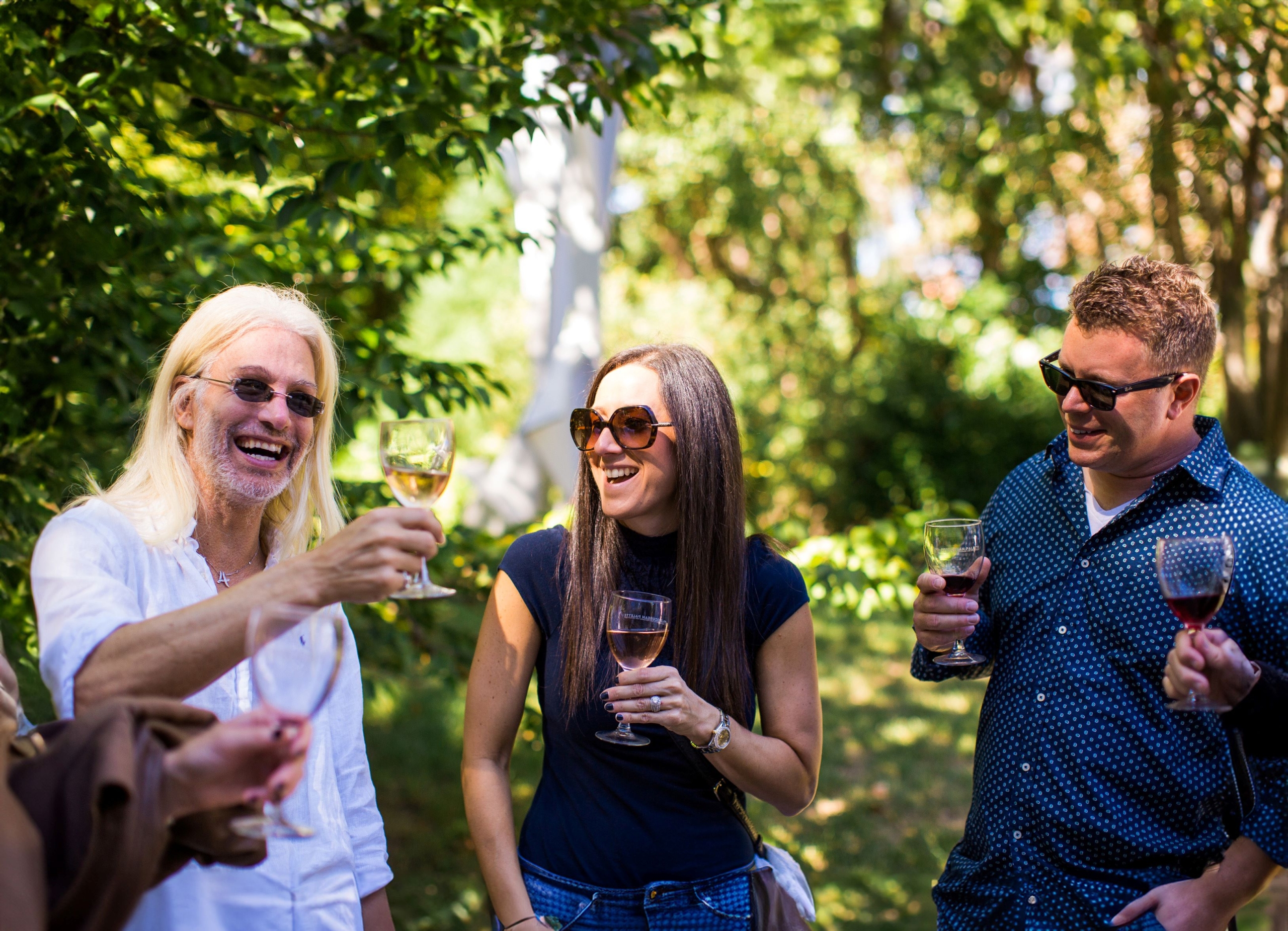 Two men and a woman standing outside holding glasses of wine.