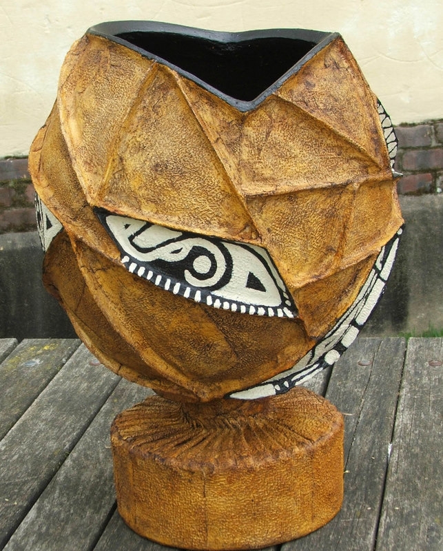 A oval shaped vessel painted tan, with black and white designs on it.