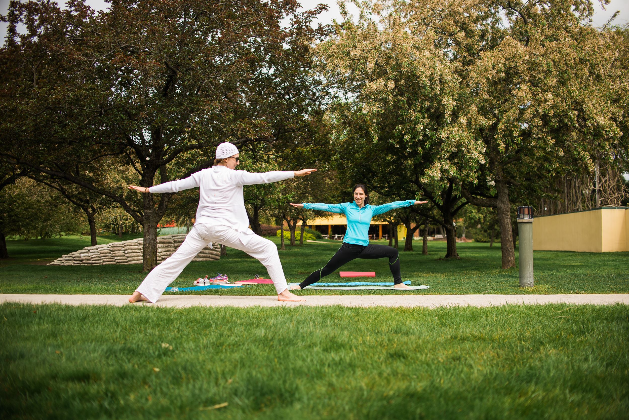 Two women doing a standing yoga pose outside underneath the crabapple trees.