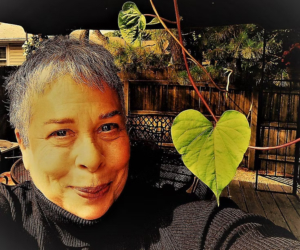 A selfie of Lesley Parnass smiling with a green heart shaped leaf.
