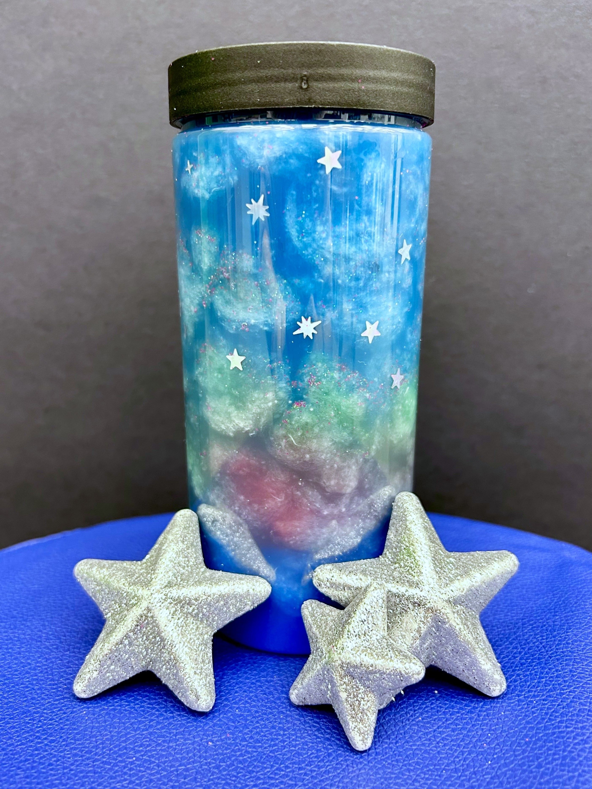 A jar of blue glittery paint and three silver stars in front of it.