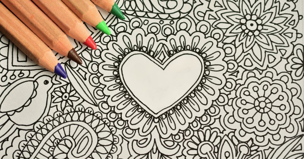 A black and white hand drawn heart with designs around it. There are five colored pencils on top of the drawing.