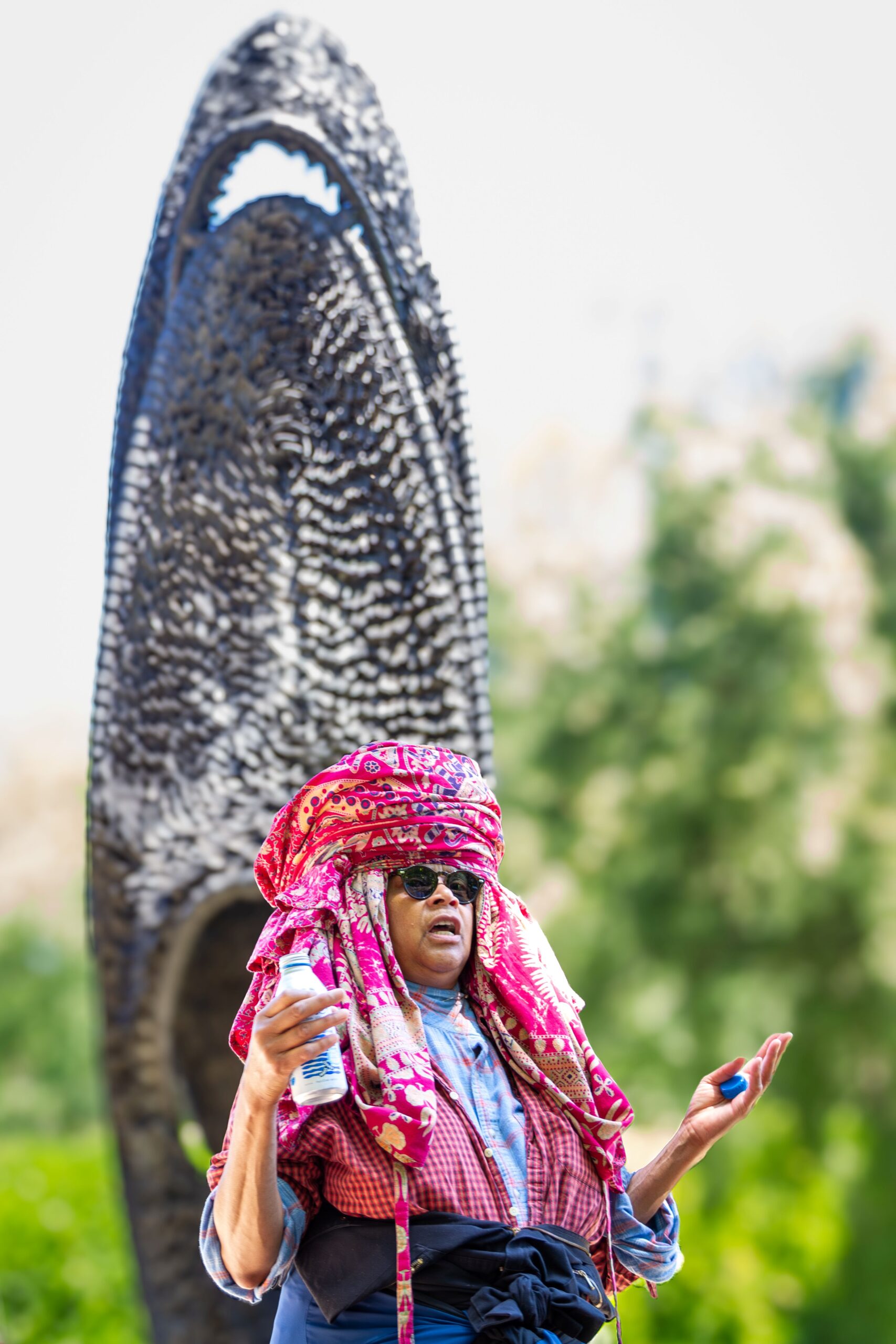 Chakaia Booker, wearing a pink headdress, speaks in front of her sculpture FOCI.