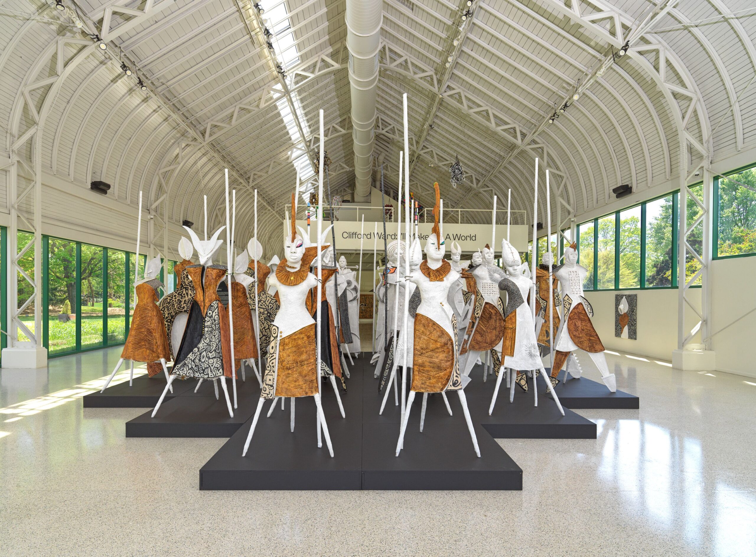Animism by Clifford Ward. 24 totemic figures are arranged in rows on a black pedastal.