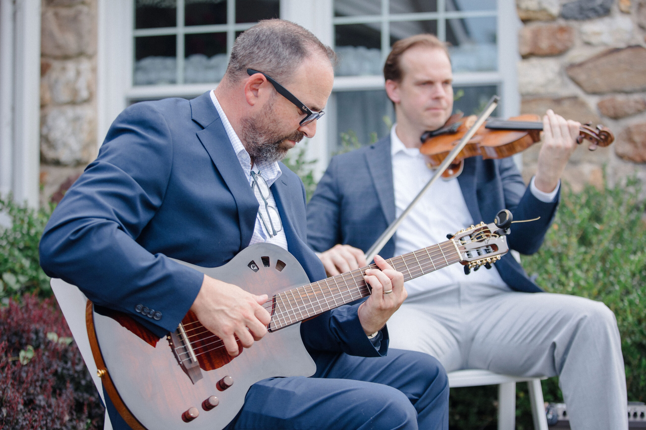 The Midnighters- two men in suits with a guitar and violin- perform outdoors.
