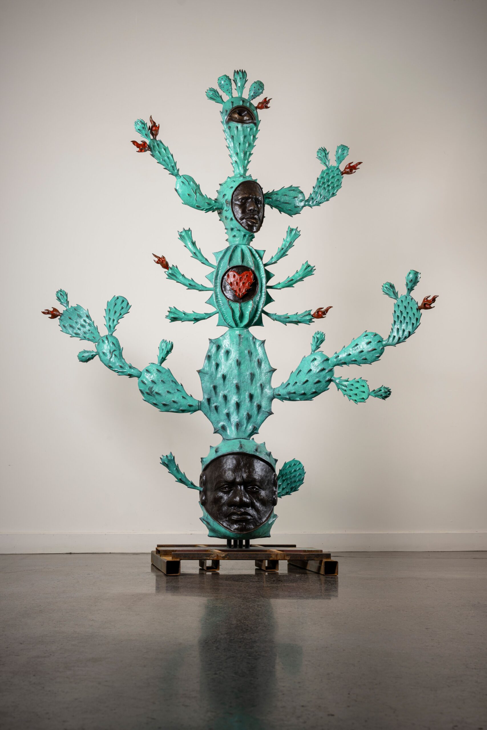 A tall green cactus sculpture with two heads built into it.