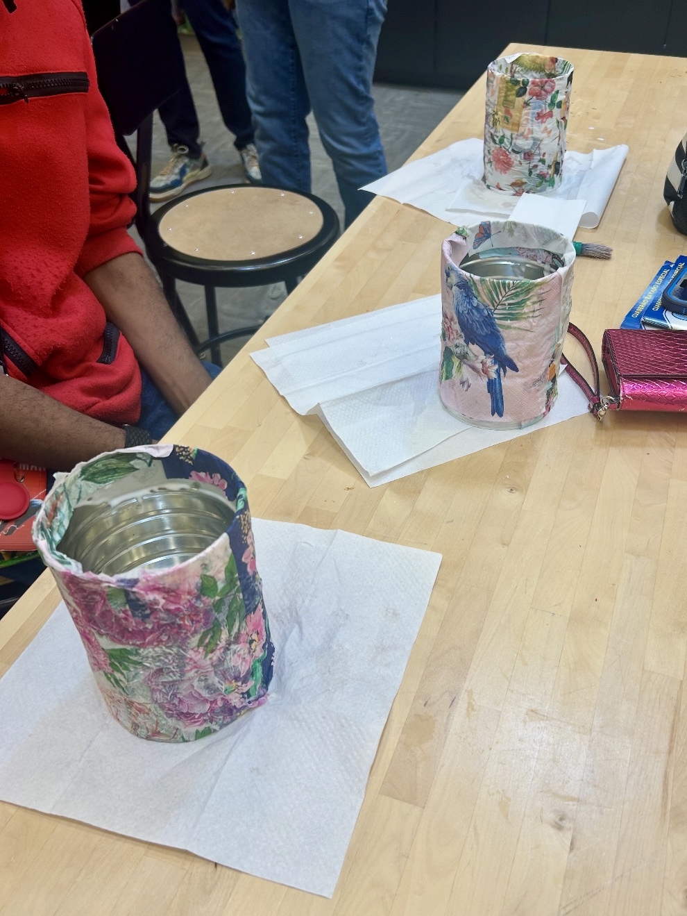Three recycled coffee cans on a table with colorful designs painted on them.