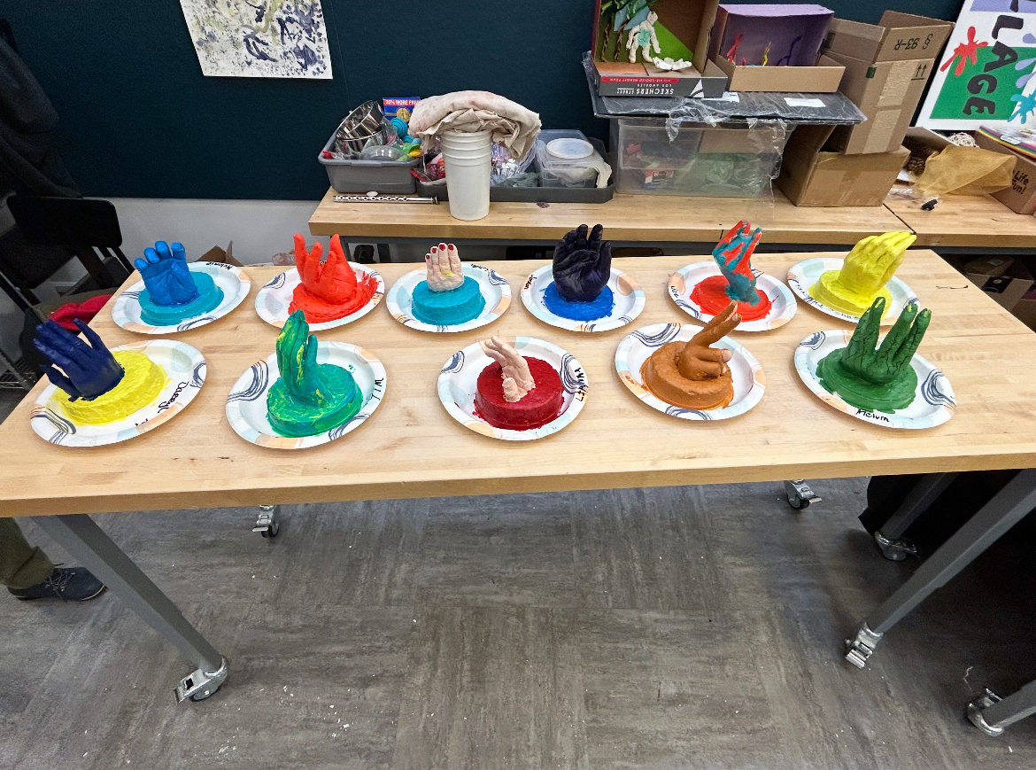 Eleven painted plaster molds of hands on a table.