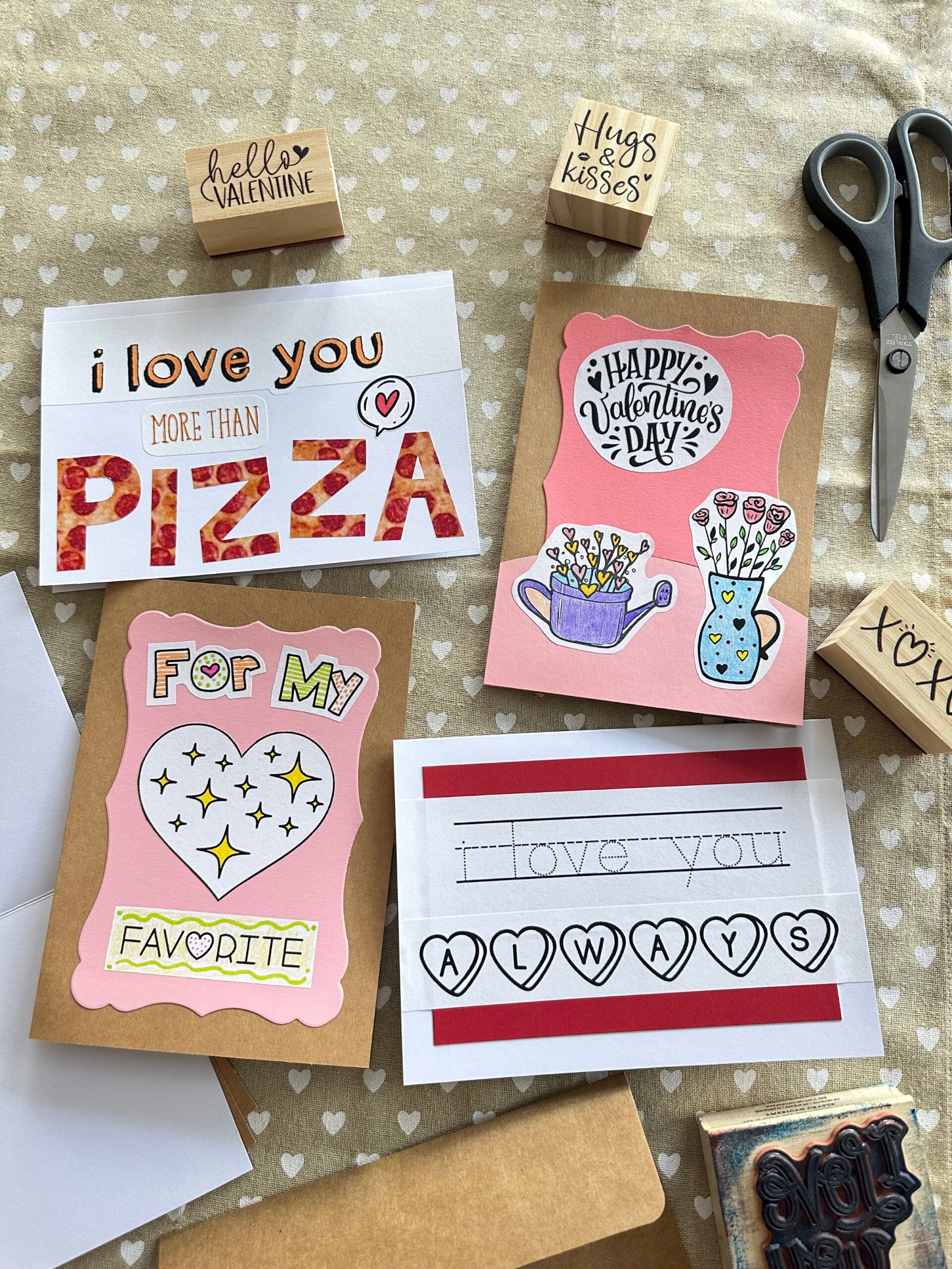 Four handmade Valentines cards and stamps on a tablecloth.