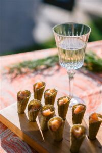A crystal glass of wine and cone shaped appetizers with salmon on a serving tray.