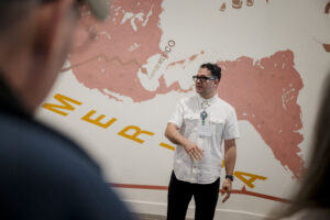 Artist Salvador Jiménez-Flores speaking in front of his mural 'Memoria, Tierra, Trabajo: A Glimpse of the Semiquincentennial.