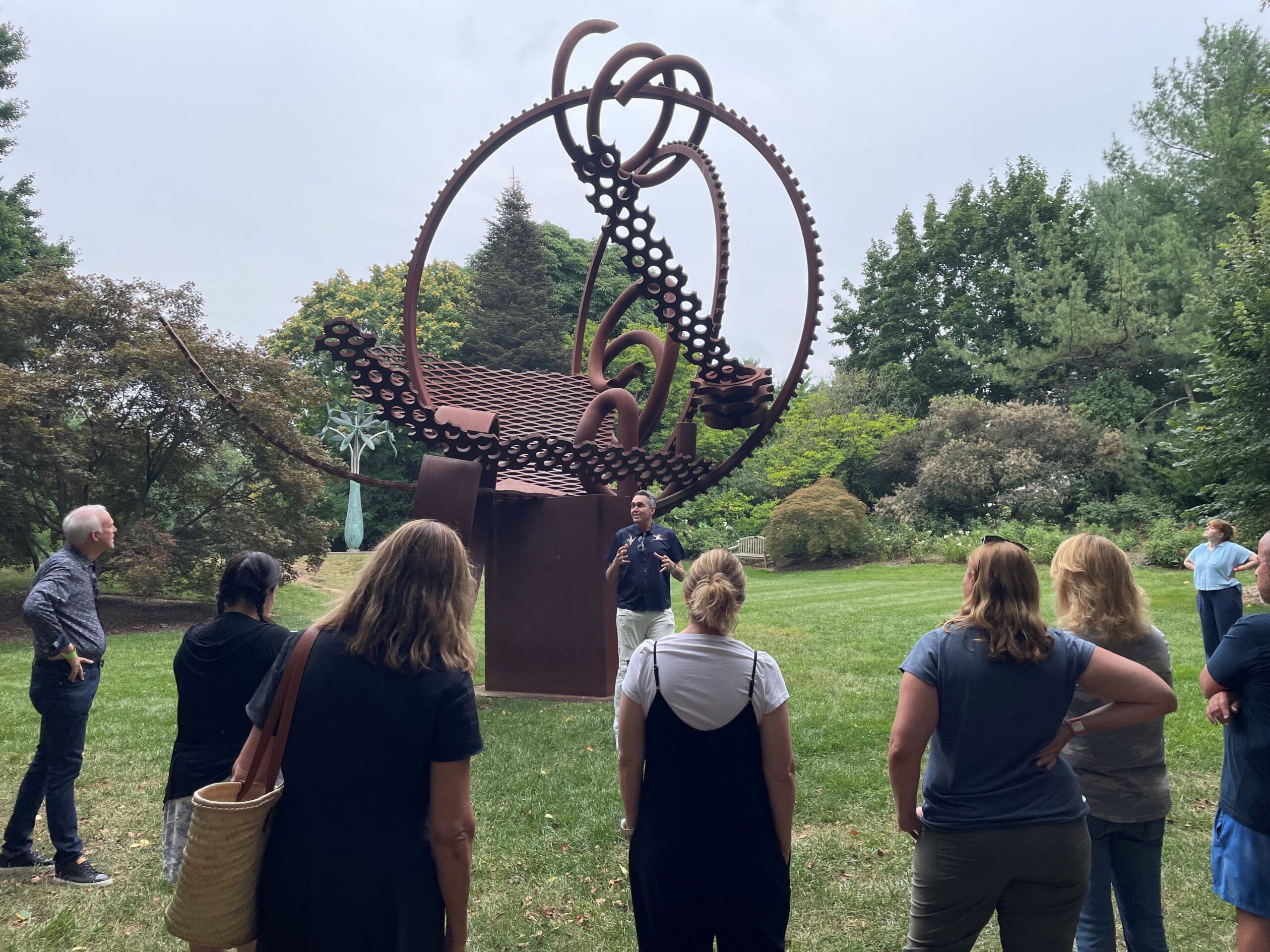 A man speaks to a group of teachers in front of Harp of David #1, a large bronze sculpture.