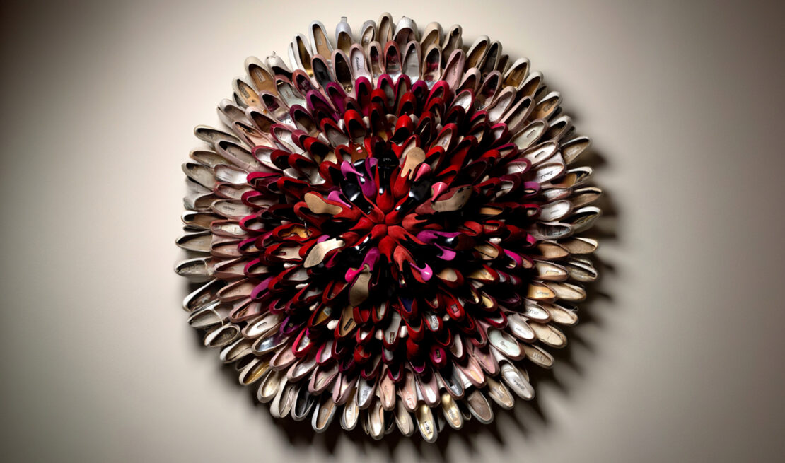 Circular wall sculpture made from nested high-heeled shoes in red, pink, and beige tones on a neutral wall