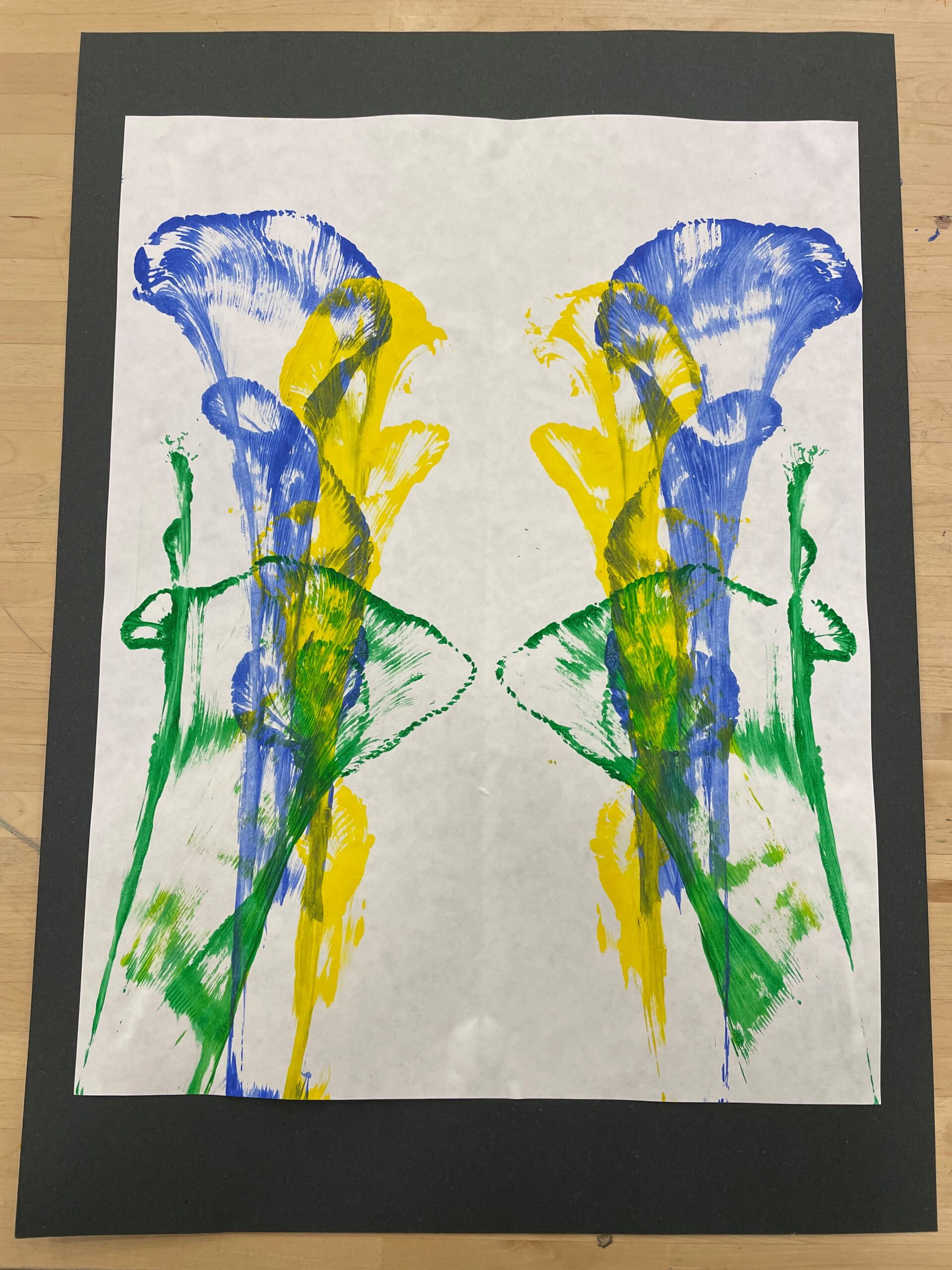 Yellow, green, and blue string painting designs on a white piece of paper.