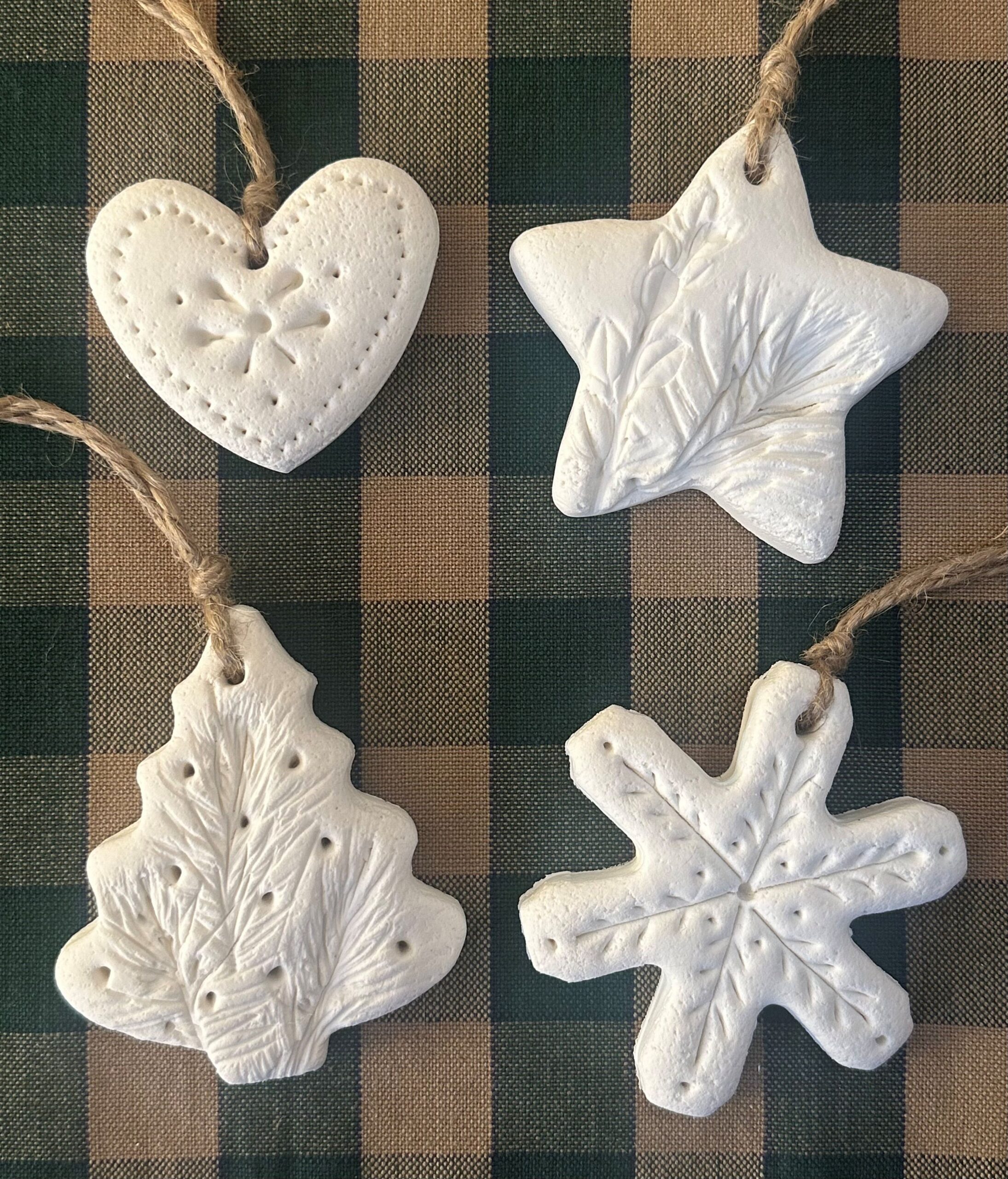 Four white clay ornaments shaped like a heart, a star, an evergreen tree, and a snowflake.