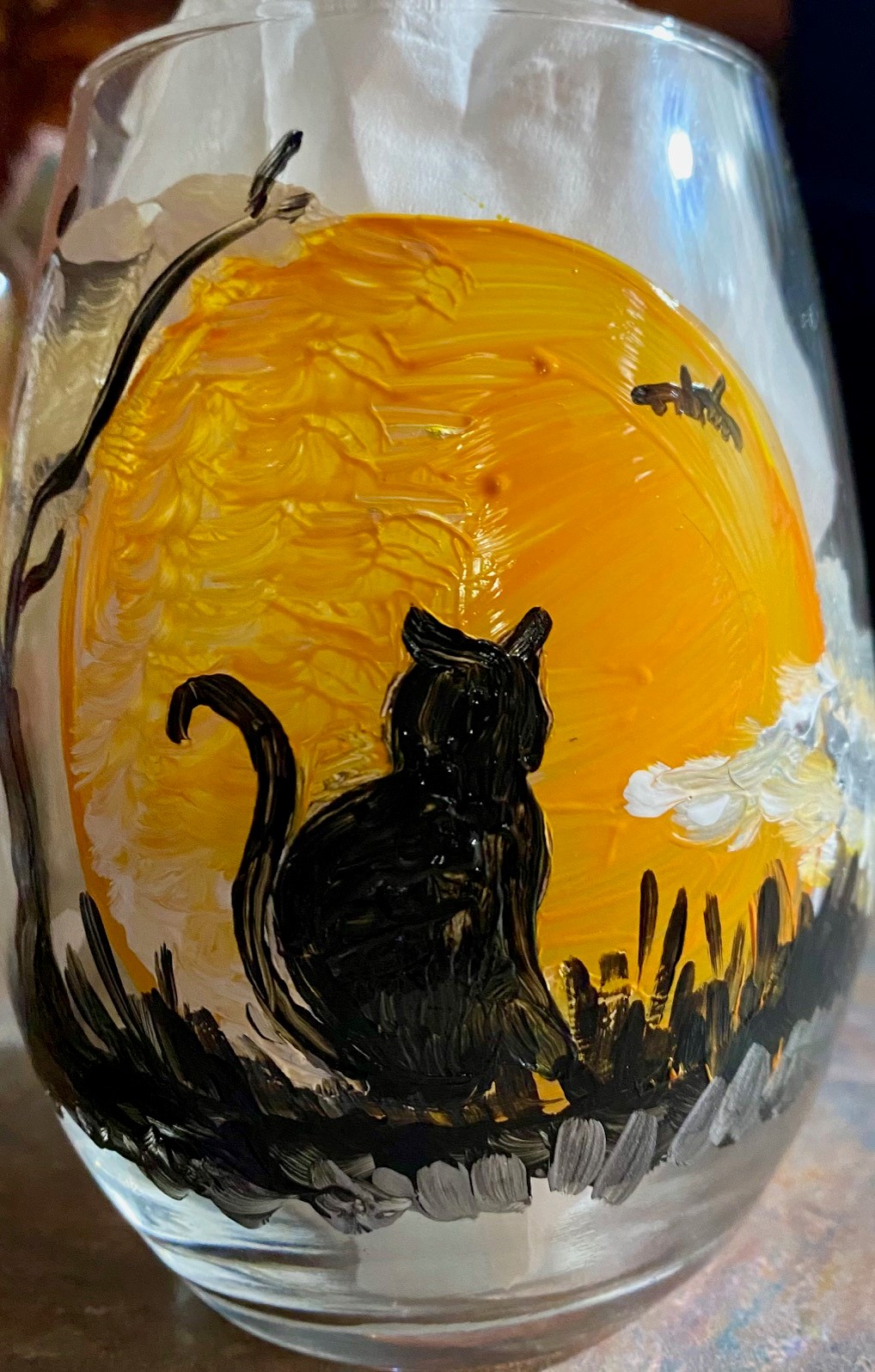 A painted wine glass with a black cat in front on an orange moon.