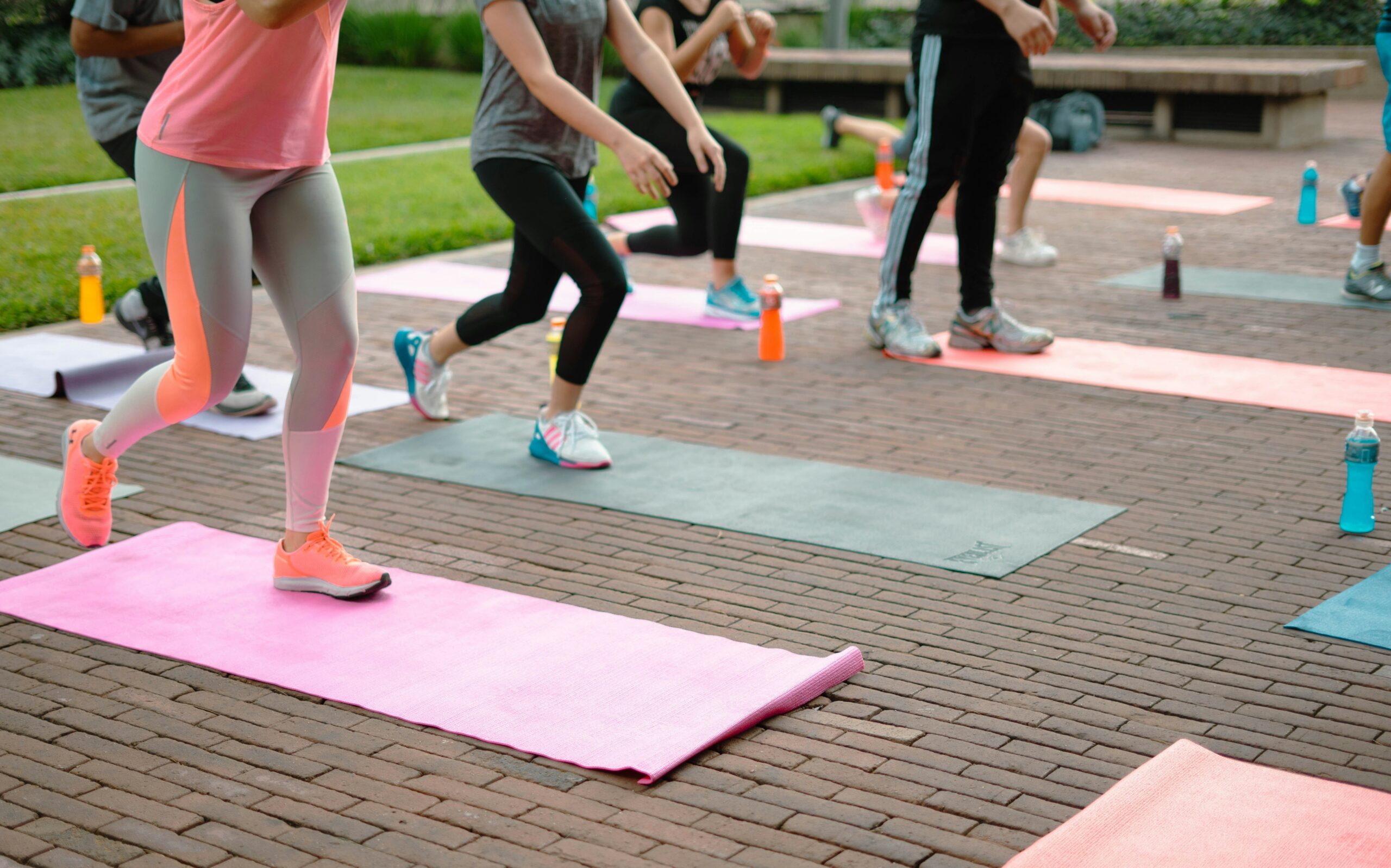 A group of people doing Zumba exercises on colorful yoga mats outside.